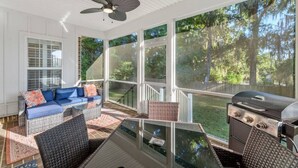 A covered outdoor area with a sofa, grill, and large windows overlooking a wooded area. - Serene Smart Home, Big Backyard, PET FRIENDLY! (Tallahassee)