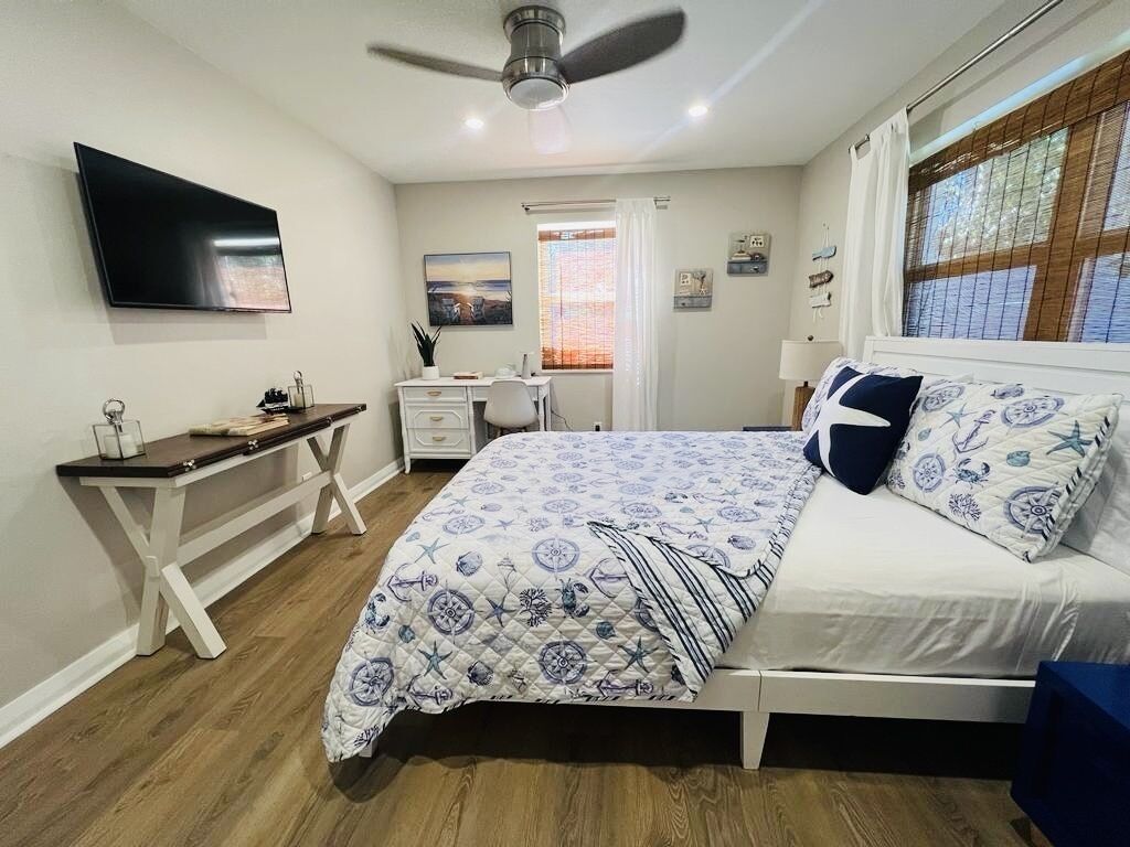 Ein Schlafzimmer mit einem Bett, einem Schreibtisch, einem Stuhl, einem Fernseher und einem Fenster mit Vorhängen.