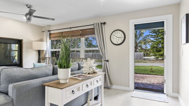 A living room with a grey sofa, a white console table with a plant, a clock, and a view of the outside.