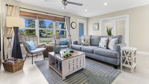 A living room with a sofa, a coffee table, a chair, a lamp, a window with curtains, and a ceiling fan.