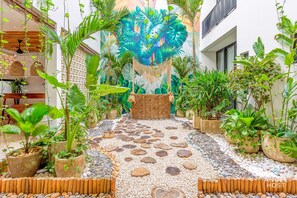 Un sentier bordé de plantes en pot dans un jardin tropical, agrémenté d’une fresque murale décorative.