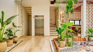 A spacious indoor area with a wooden floor, potted plants, a staircase, and a modern elevator. - Zamia Hotel Boutique (Playa del Carmen)