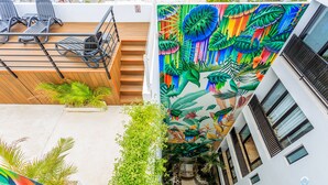A modern building with a vibrant mural of tropical leaves and flowers, outdoor seating with chairs and tables, and a stone pathway. - Zamia Hotel Boutique (Playa del Carmen)