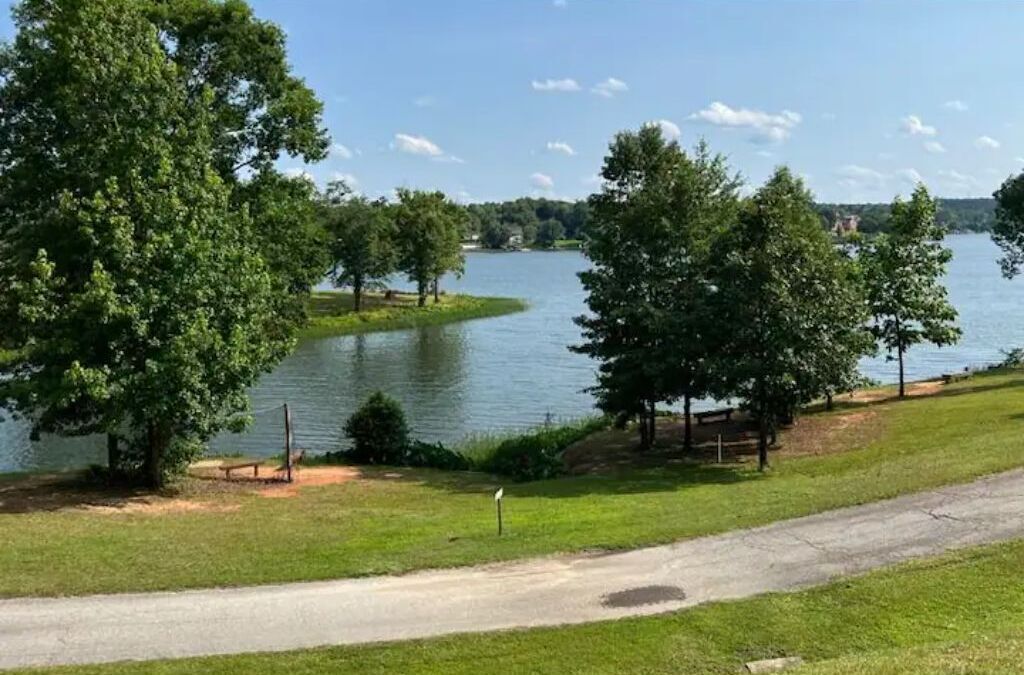 A lakeside park with a walking path, benches, and trees.
