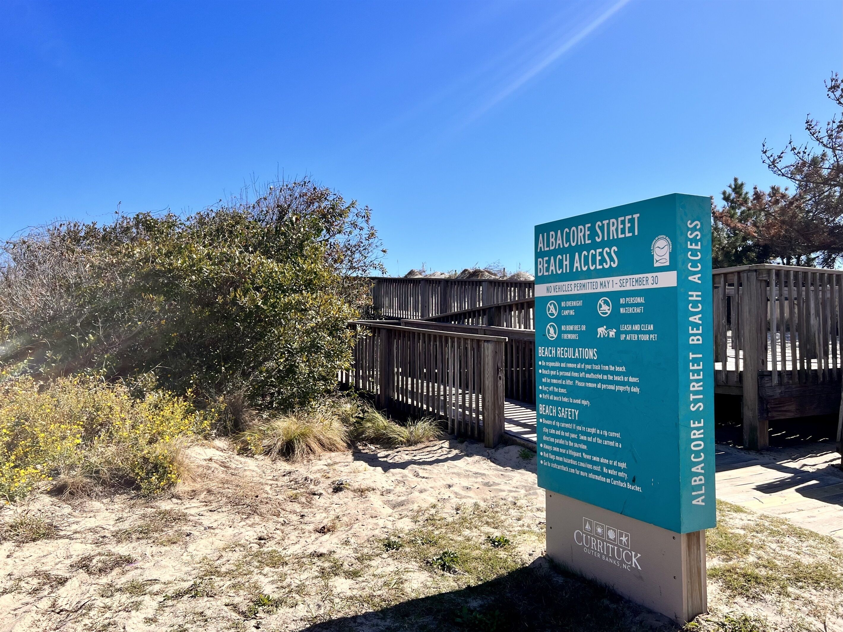 A beach access sign for Albacore Street Beach, detailing regulations and safety information.