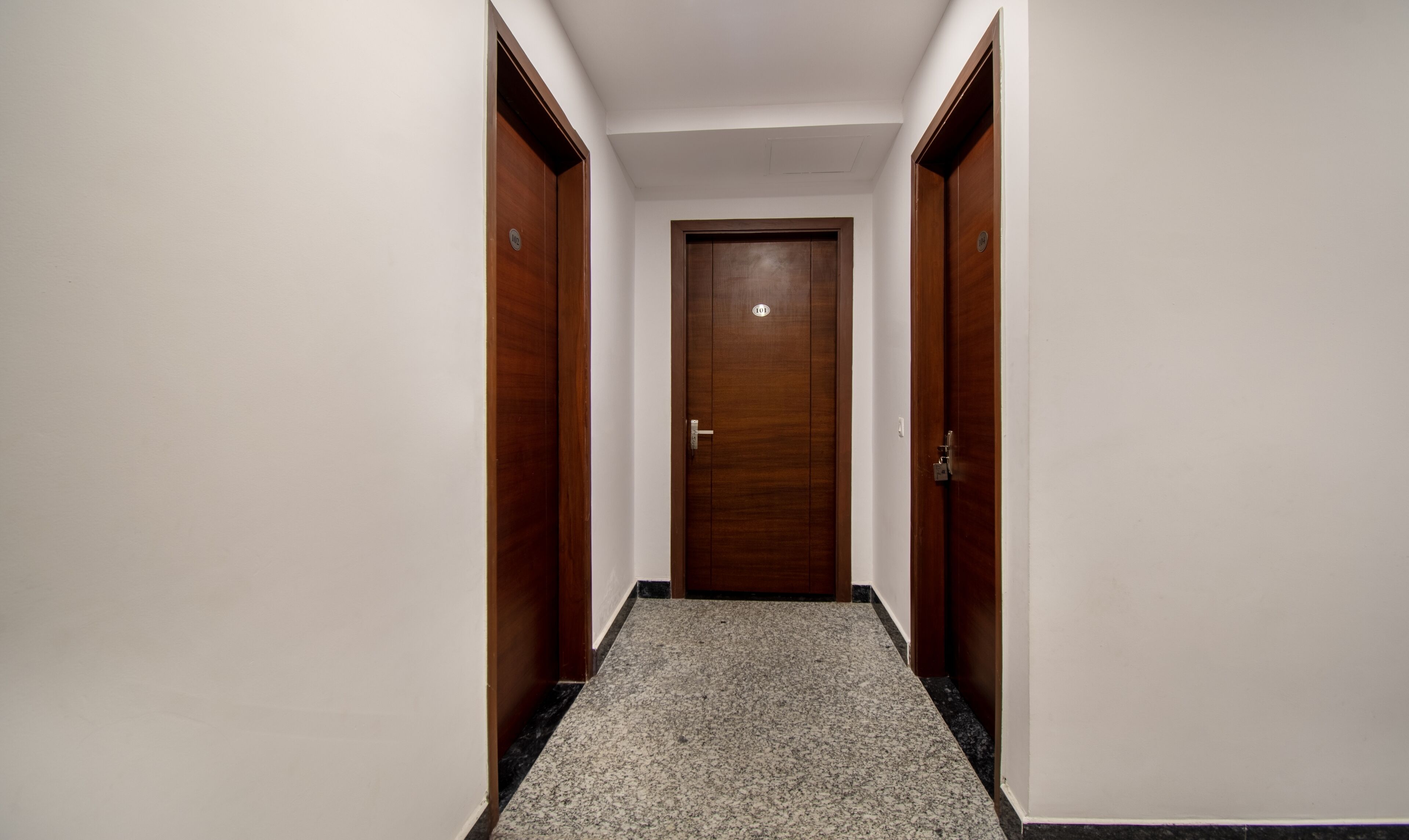 A hallway with a wooden door at the end, flanked by two wooden doors with a number plate.