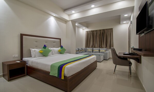 A modern hotel room with a large bed, a desk, a chair, and a TV.