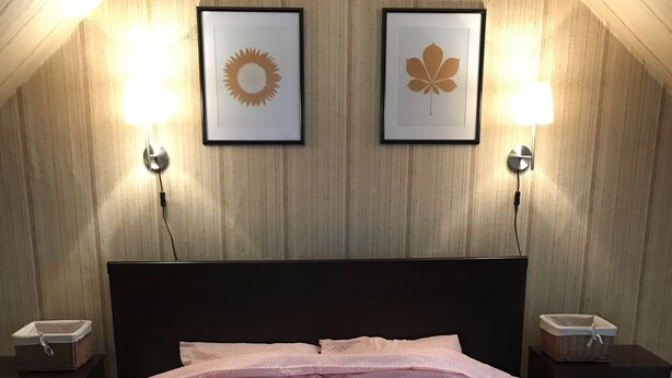 A hotel room with a bed, two wall-mounted lamps, and two framed pictures on the wall. - Traditional Jūrmala house. (Jūrmala)