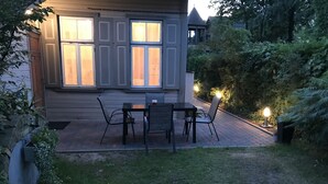 A patio with a table and chairs, a small garden area, and a house with large windows. - Traditional Jūrmala house. (Jūrmala)
