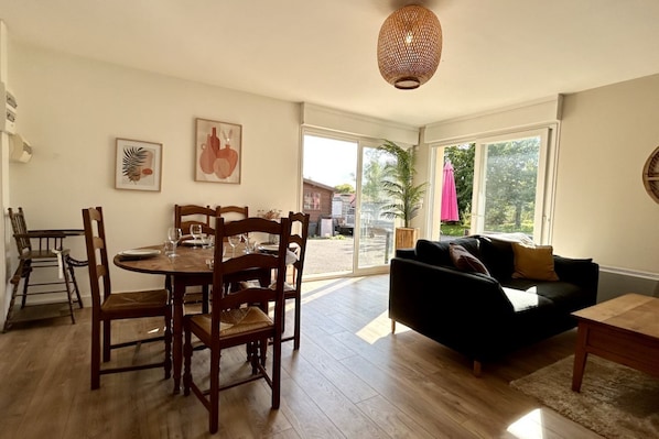 A dining area with a round table and chairs, a black sofa, and a large window with a view of the outdoors.