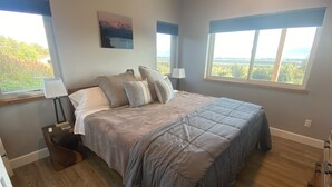 A bedroom with a large bed, two bedside lamps, a nightstand, a window with a view, and a painting on the wall. - Incredible views in Homer, AK, first floor 2BR/1BA, kitchen, pet friendly (Homer)