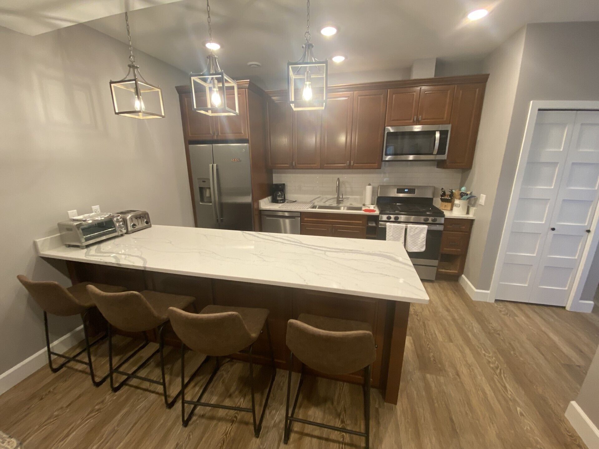 A modern kitchen with a large island, bar stools, stainless steel appliances, and wooden cabinets.