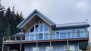 A two-story house with a large balcony, a garage, and a covered porch area. - Incredible views in Homer, AK, first floor 2BR/1BA, kitchen, pet friendly (Homer)