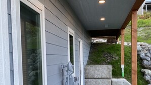 A house with a covered porch, a concrete pathway, and a stone retaining wall. - Incredible views in Homer, AK, first floor 2BR/1BA, kitchen, pet friendly (Homer)