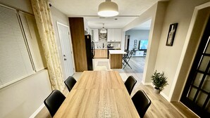 A dining area with a wooden table and black chairs, a kitchen in the background, and a potted plant on the floor. - Siesta Beach Getaway - Minutes to Beach, Shops, Dining (Sarasota)