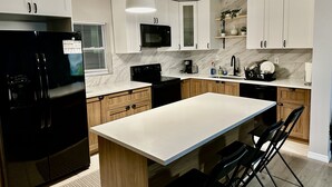 A modern kitchen with white cabinets, a black refrigerator, a central island, and black bar stools. - Siesta Beach Getaway - Minutes to Beach, Shops, Dining (Sarasota)