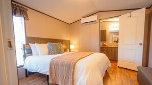 A bedroom with a bed, bedside tables, a lamp, an air conditioning unit, a mirror, and a door leading to a bathroom. - Dog friendly peaceful retreat for 2 (Concho)