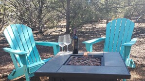 A table with two turquoise Adirondack chairs, a bottle of wine, and two glasses. - Dog friendly peaceful retreat for 2 (Concho)