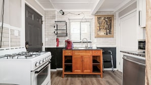 A compact kitchen with white brick walls, a gas stove, a sink, and wooden cabinets. - Bill Murray - Private Barcade and Outdoor Lounge - OSU/Clintonville/CrewStadium (Columbus)