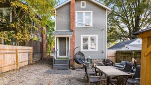 A two-story house with a grey exterior, a brick chimney, and a small front porch with a swing chair. - Bill Murray - Private Barcade and Outdoor Lounge - OSU/Clintonville/CrewStadium (Columbus)
