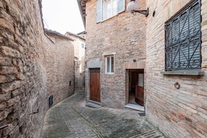 A narrow alleyway with stone buildings, a wooden door, and a metal gate.