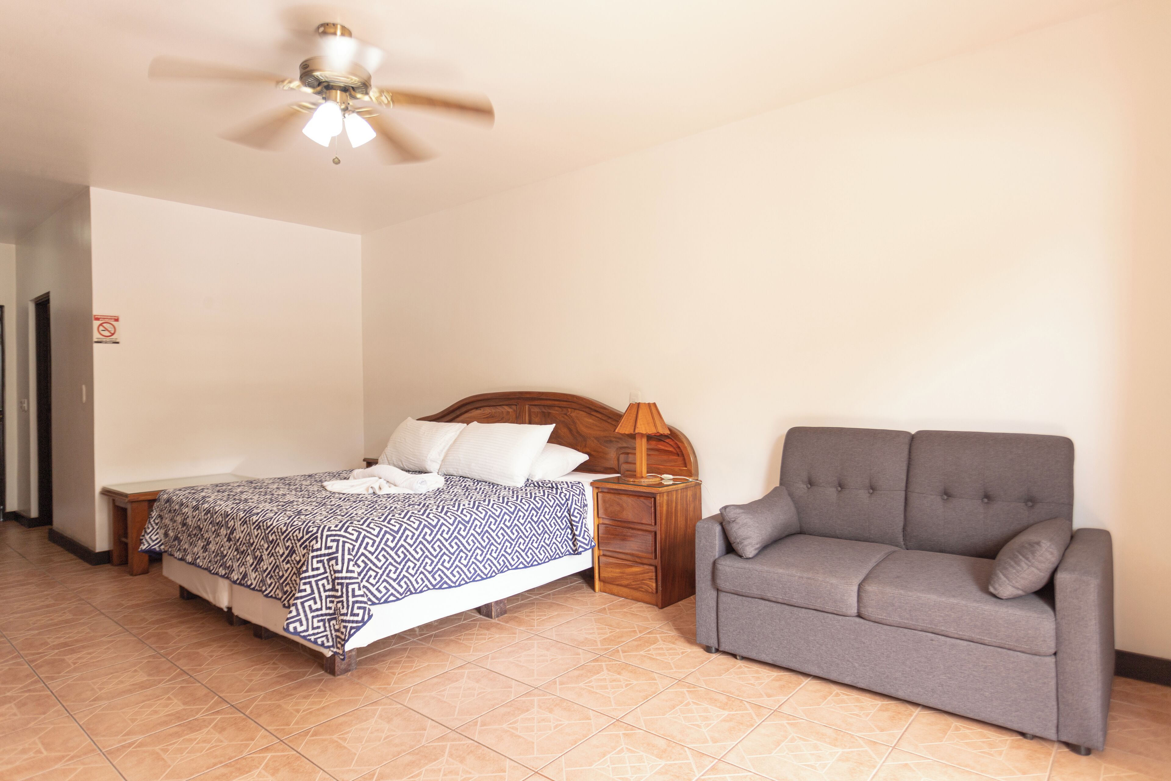 Un dormitorio con una cama, una mesita de noche, un sofá y un ventilador de techo.
