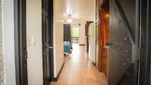 A hallway with a bed, a ceiling fan, and a large metal door. - Inn on the Park (Quepos)