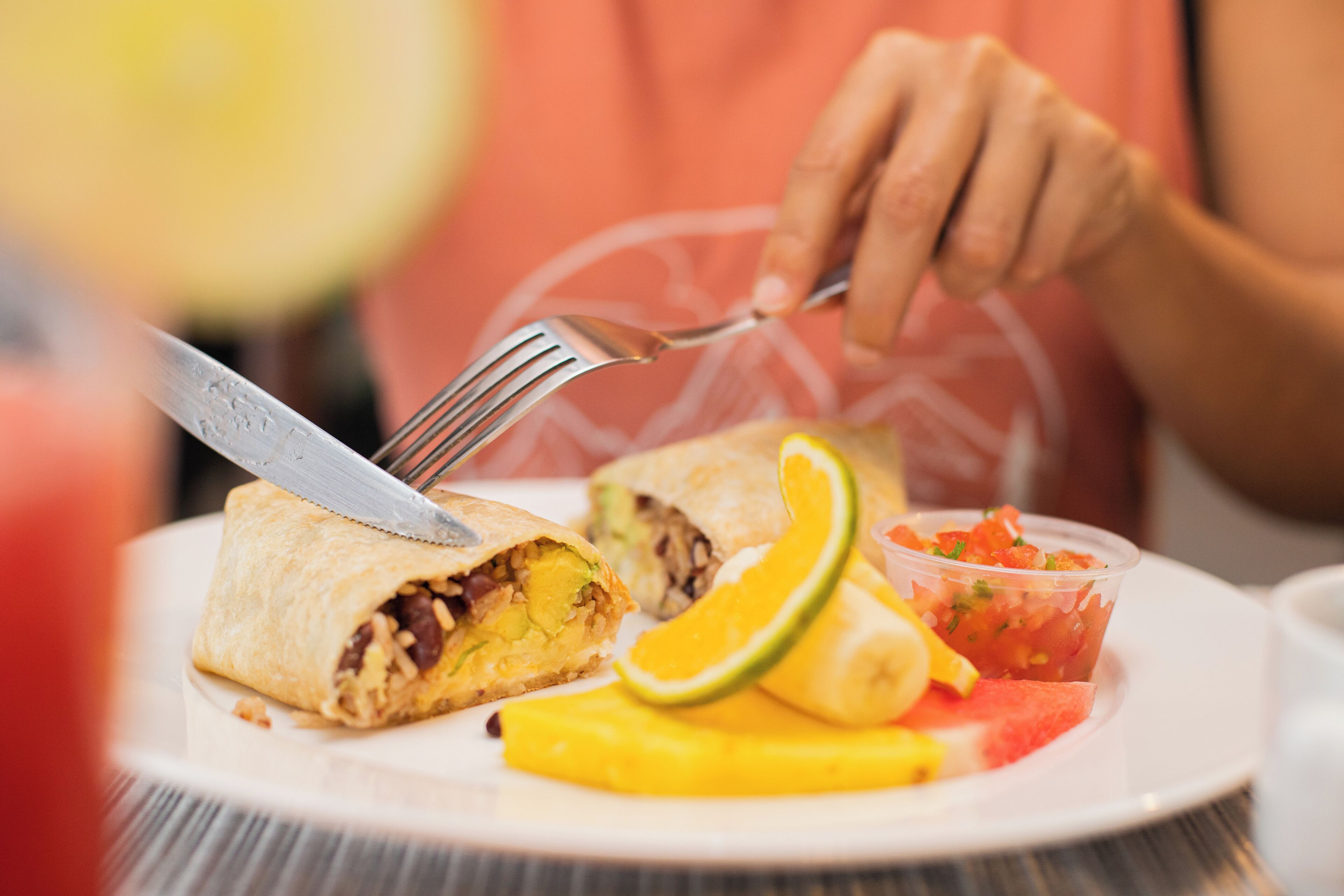 Une assiette contenant un burrito, une tranche de mangue, une tranche de pastèque et un petit récipient de salsa.