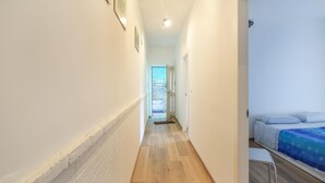 Un estrecho pasillo con suelo de madera que conduce a un dormitorio con cama y ventana.