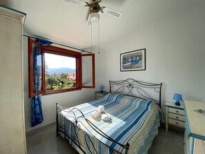 Een slaapkamer met een bed, een nachtkastje, een bureau, een raam met uitzicht en een plafondventilator.