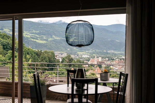 Un balcon avec une table et des chaises, un luminaire suspendu et une vue sur une ville et des montagnes.