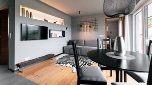 A modern living room with a flat-screen TV, a dining table with chairs, a sofa, a zebra rug, and a decorative wall piece. - Apartment 'Cityview Apt 1' with Mountain View, Private Terrace and Wi-Fi (Bressanone)