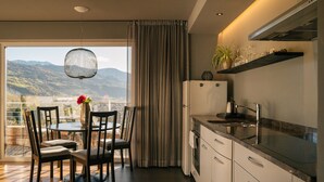 A modern kitchen with a view of mountains, a dining area with chairs and a table, and a large window with curtains. - Apartment 'Cityview Apt 1' with Mountain View, Private Terrace and Wi-Fi (Bressanone)