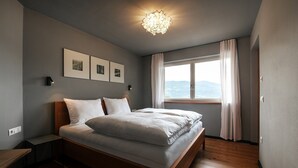 A bedroom with a bed, a nightstand, a wall-mounted light fixture, and a window with curtains. - Apartment 'Cityview Apt 1' with Mountain View, Private Terrace and Wi-Fi (Bressanone)