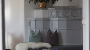 A room with a white wall, a grey cabinet, a plant in a gold pot, and a white fur throw on a dark sofa.