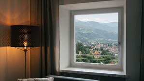 A room with a view of a town and mountains through a window, a lamp, and a sofa.