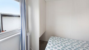 Une pièce avec un lit, une fenêtre avec des rideaux et un radiateur.