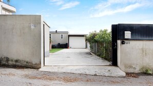 Une allée menant à un garage, avec un mur en béton sur la gauche et une clôture noire sur la droite.