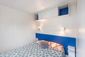 Un dormitori amb un llit, una tauleta de nit, una estant penjada a la paret i un capçal blau.