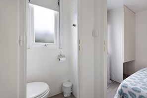A small, clean bathroom with a toilet, a window, and a white cabinet. - Mobile Home "Villa Granja Sol 1" with Shared Garden & Wi-Fi (São Felix da Marinha)