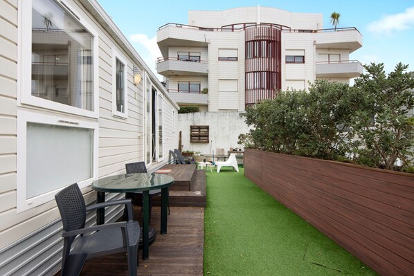 A residential building with a patio area featuring a table and chairs, a wooden deck, and a green artificial lawn. - Mobile Home "Villa Granja Sol 1" with Shared Garden & Wi-Fi (São Felix da Marinha)