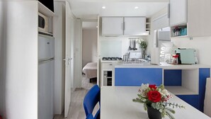 A compact kitchen with white cabinets, a blue countertop, and a dining area with a chair and a vase of flowers. - Mobile Home "Villa Granja Sol 2" with Shared Garden & Wi-Fi (São Felix da Marinha)