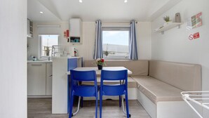 A compact kitchen with a dining area, a sofa, and a window with curtains. - Mobile Home "Villa Granja Sol 2" with Shared Garden & Wi-Fi (São Felix da Marinha)