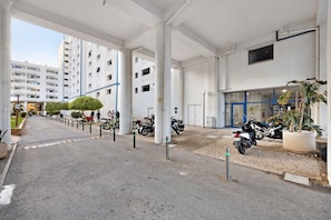 A parking area with motorcycles, a building entrance, and a clear sky.