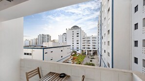 A balcony with a wooden table and chairs, overlooking a cityscape with modern buildings and a small green area. - Apartment "Clube Praia da Rocha 3" with Balcony & Wi-Fi (Portimao)
