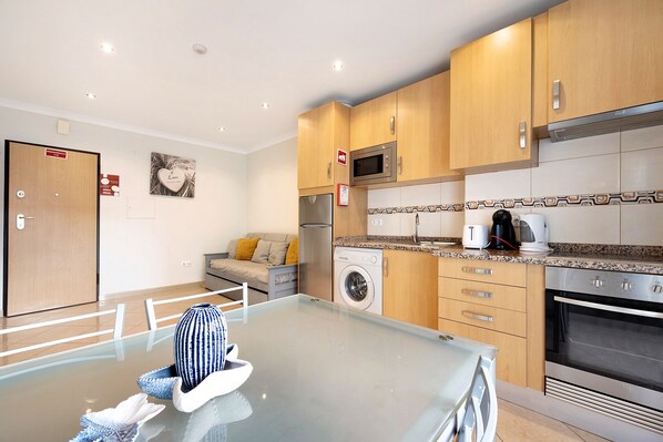 A modern kitchen with wooden cabinets, a stainless steel refrigerator, a microwave, a washing machine, and an oven.