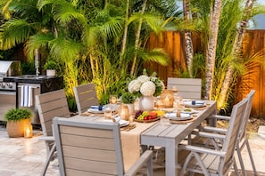 An outdoor dining area with a table set for four, surrounded by chairs, with a wooden fence and lush greenery in the background. - Family Fun Villa | Heated Pool | Arcade & Ping Pong | BBQ | Near Hollywood Beach (Hollywood)