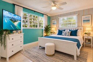 Une chambre à coucher comprenant un lit, un téléviseur, un ventilateur de plafond et une fenêtre avec des stores.