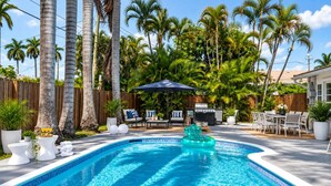 Una piscina con borde de mosaico azul, rodeada de palmeras y una valla de madera.