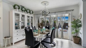 Un coin repas comprenant un buffet blanc, des chaises noires, une table en verre et un lustre.
